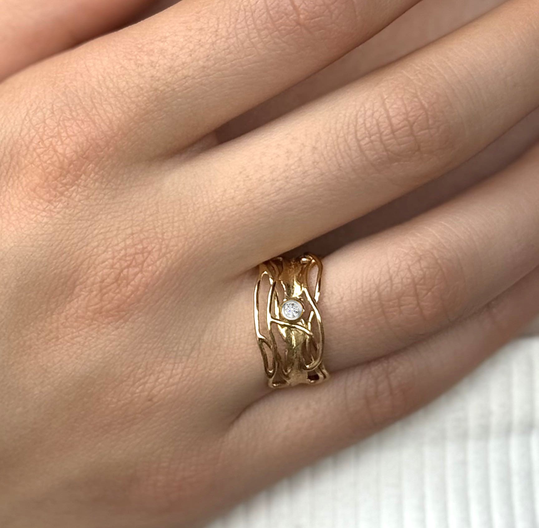 Gold ring with a diamond on a person's finger against a neutral background