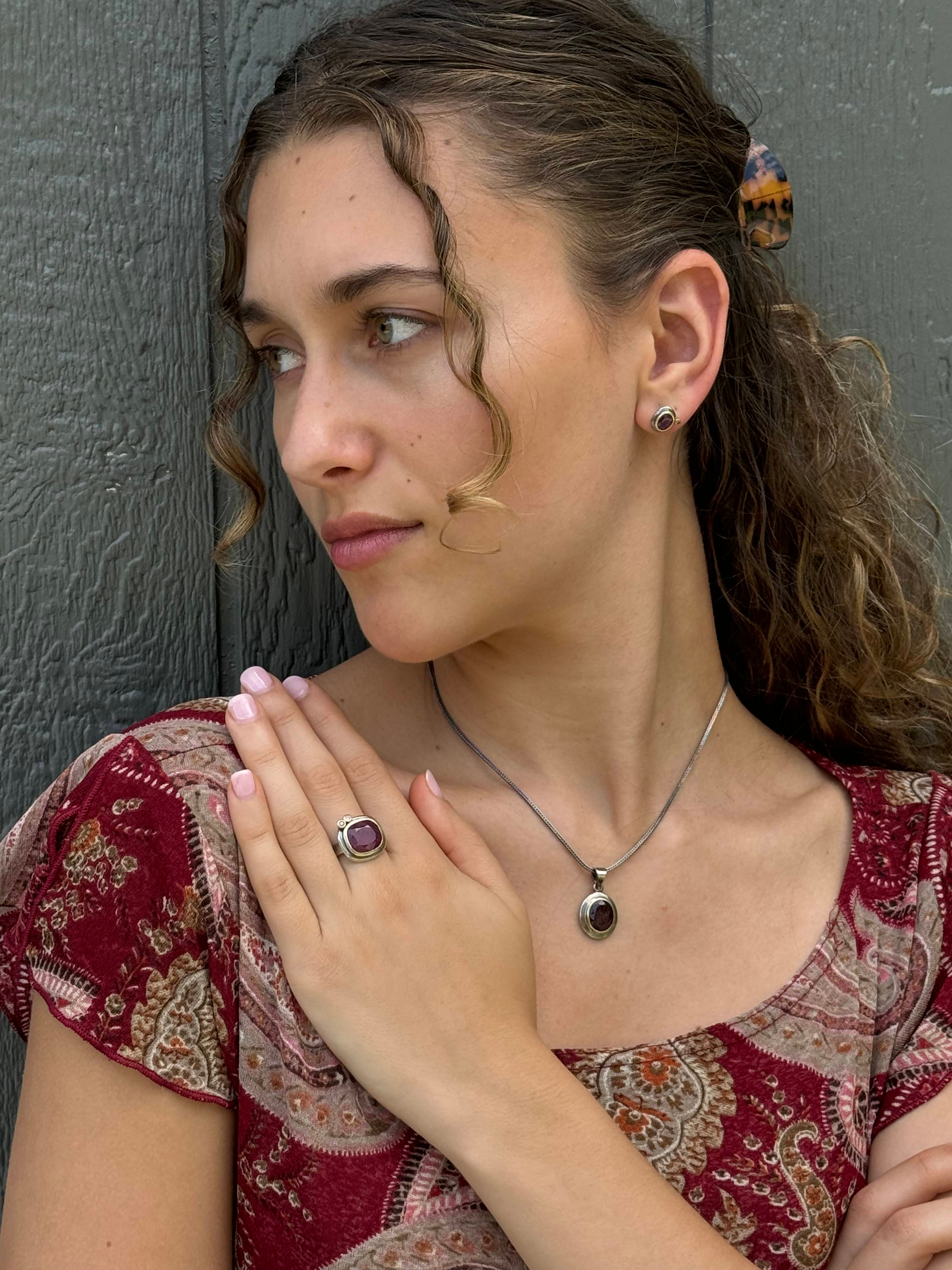 A woman wearing a sterling silver jewelry set with a faceted ruby slice, set in a 14k gold bezel, with champagne diamond accents.