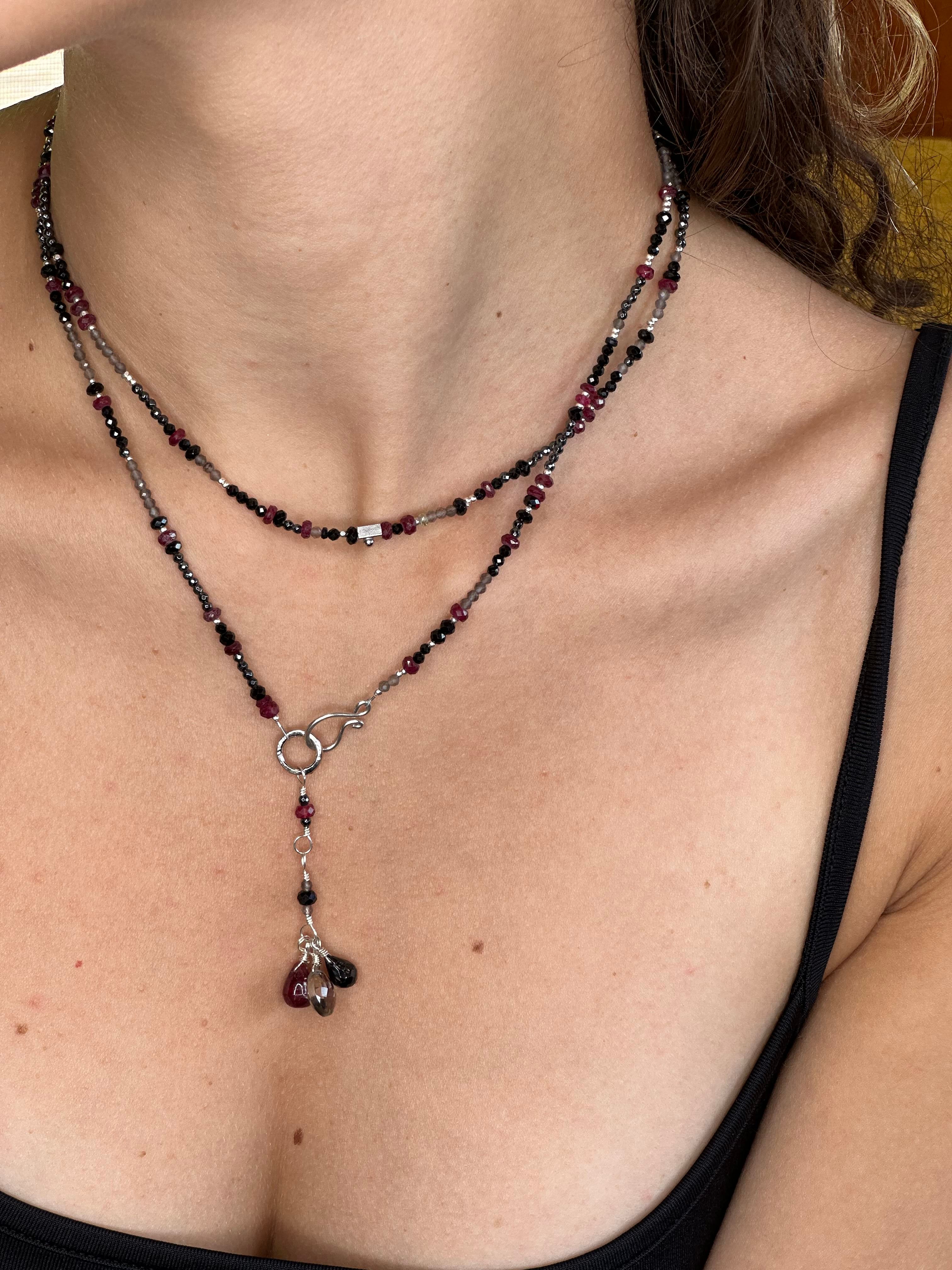 A woman wearing a necklace with a silver clasp, featuring a variety of beads including rubies, spinels, hematite, labradorite, and grey topaz.