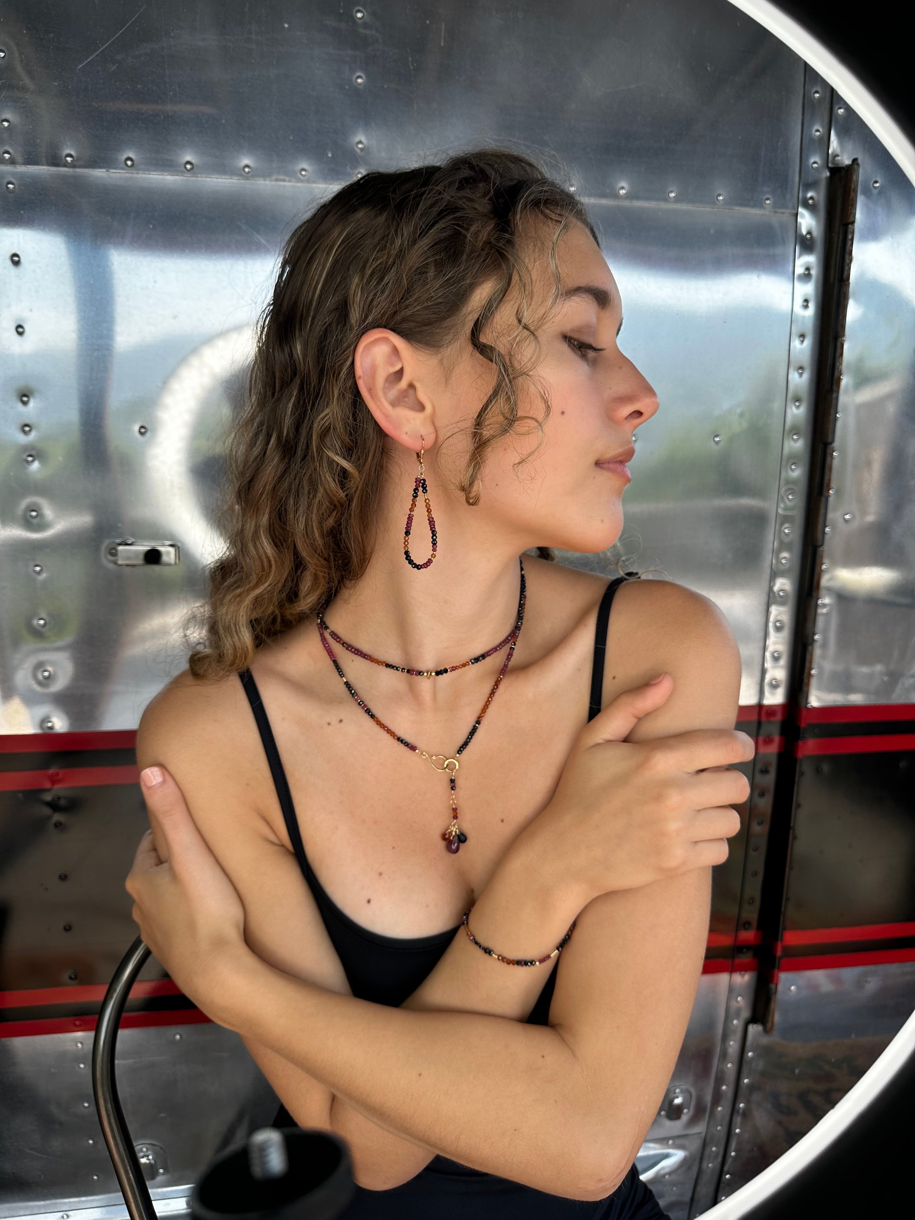 Close-up of a woman wearing multiple gemstone beaded earrings, necklaces, and a bracelet