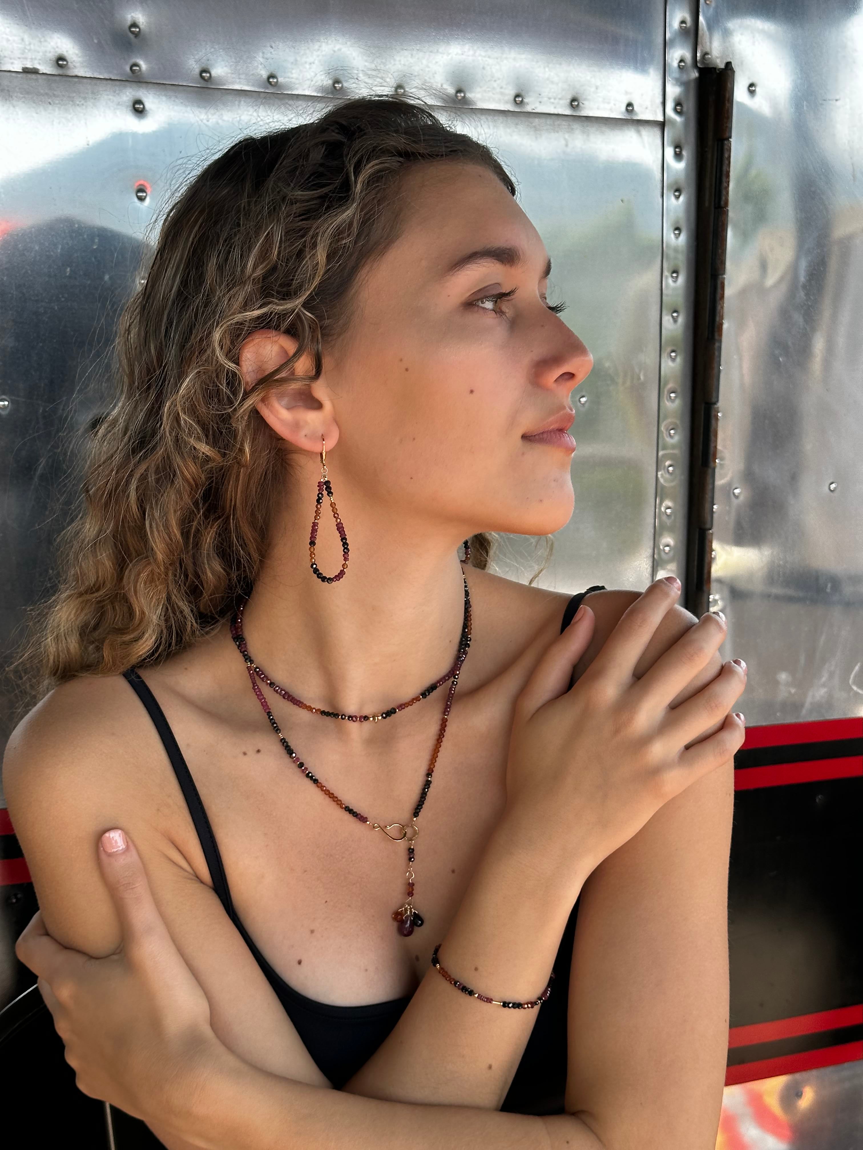 Close-up of a woman wearing multiple gemstone beaded earrings, necklaces, and a bracelet