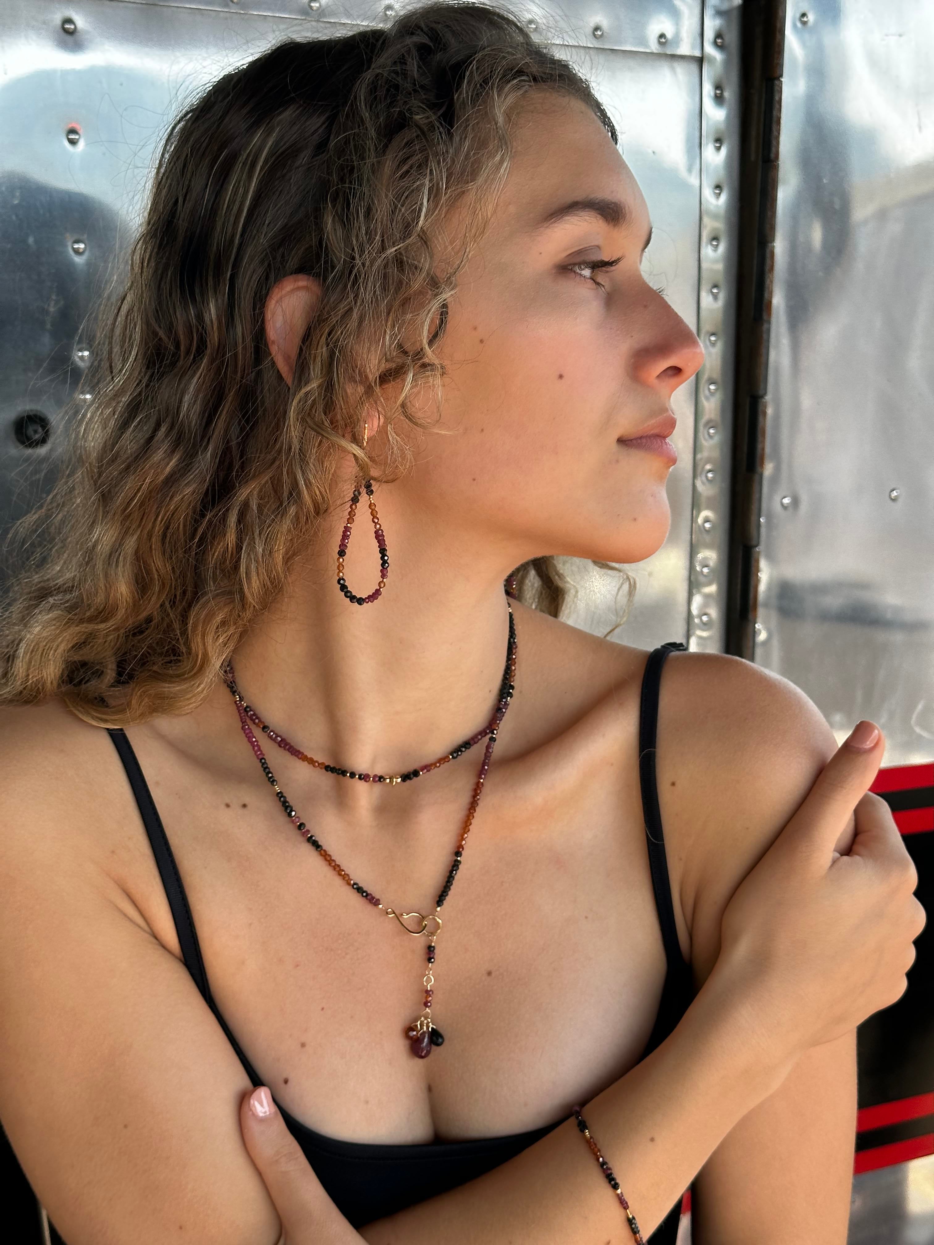 Close-up of a woman wearing multiple gemstone beaded earrings, necklaces, and a bracelet