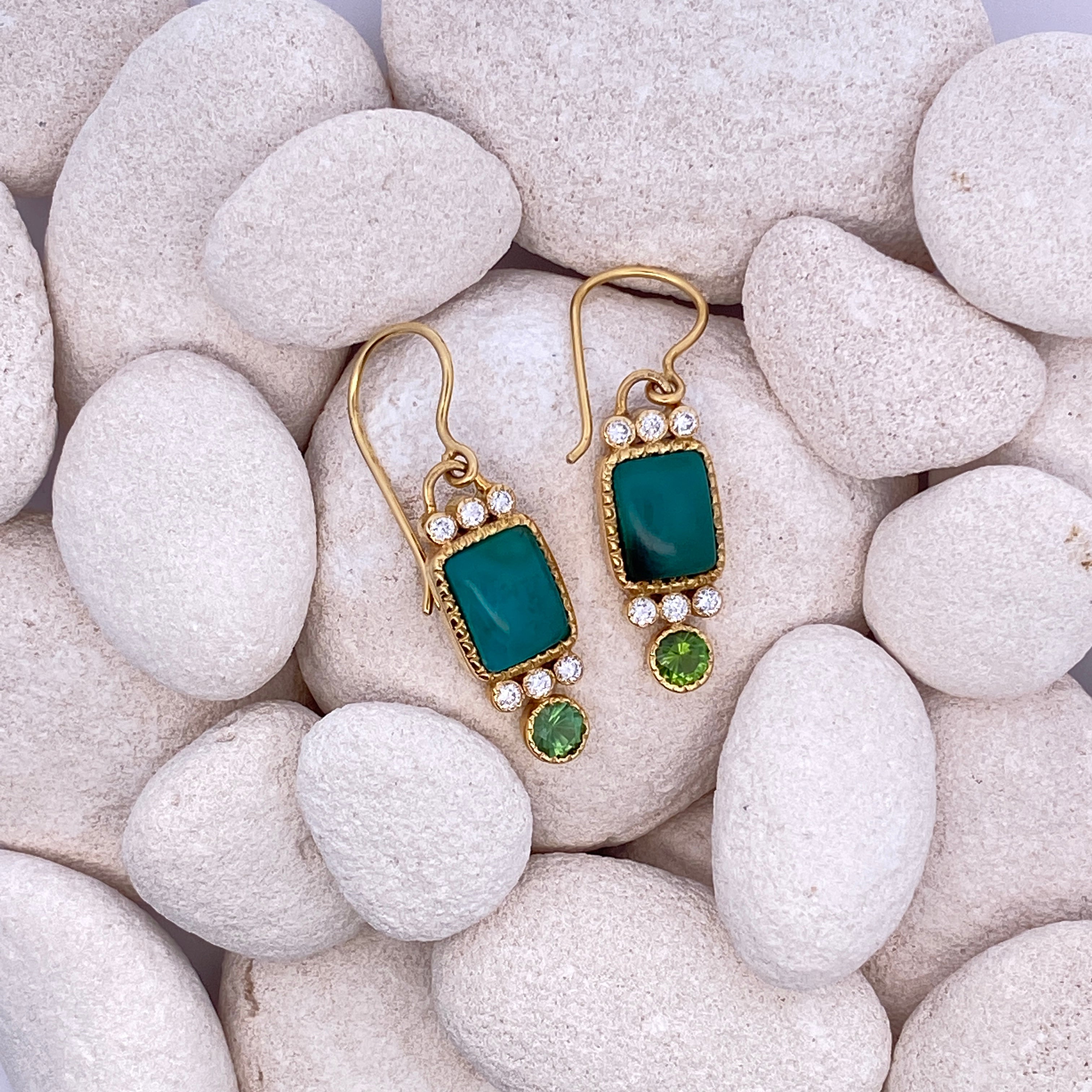 Pair of gold earrings with green gemstones on a bed of white stones