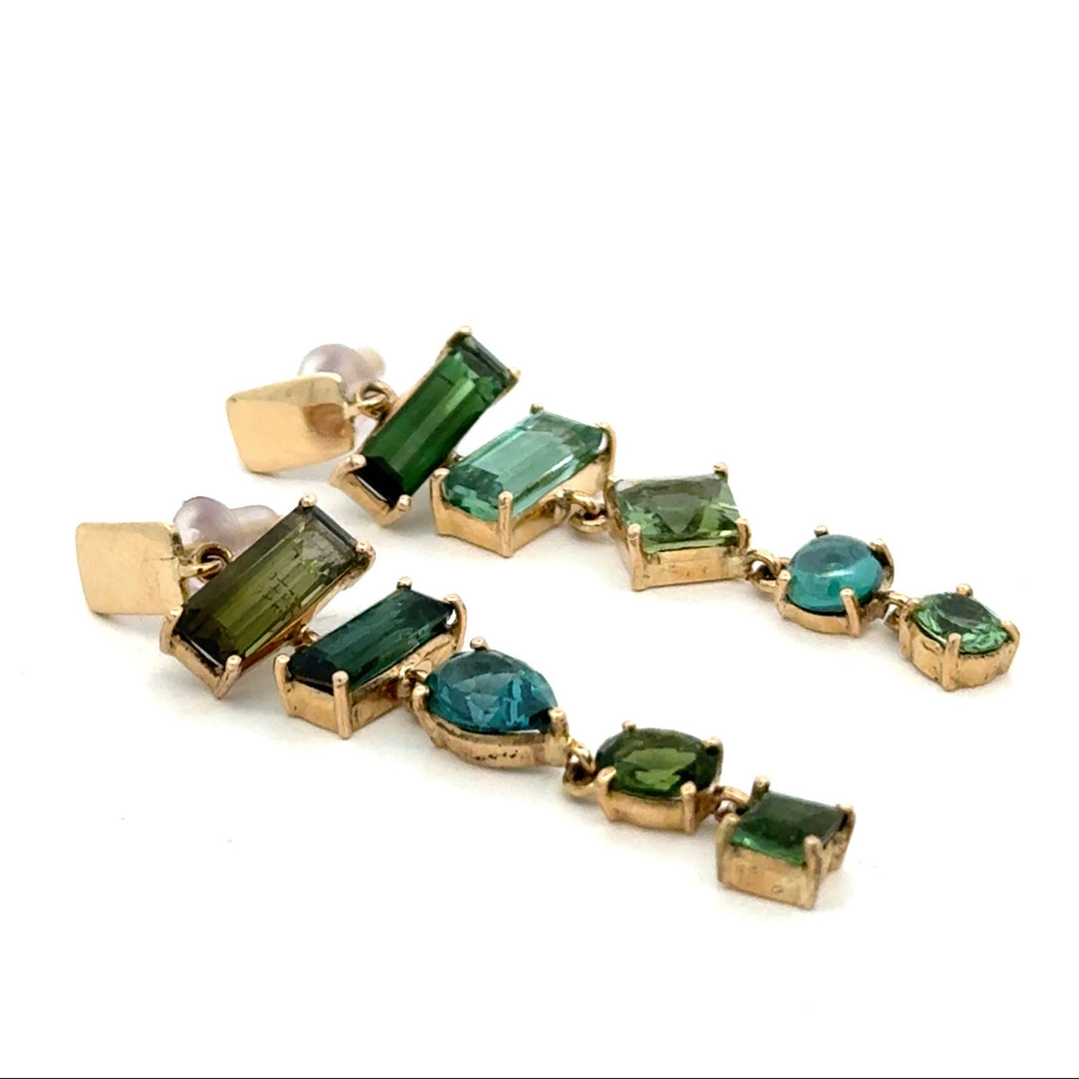 A pair of gold dangle earrings featuring a series of rectangular green and blue-green gemstones, photographed on a clean white background.