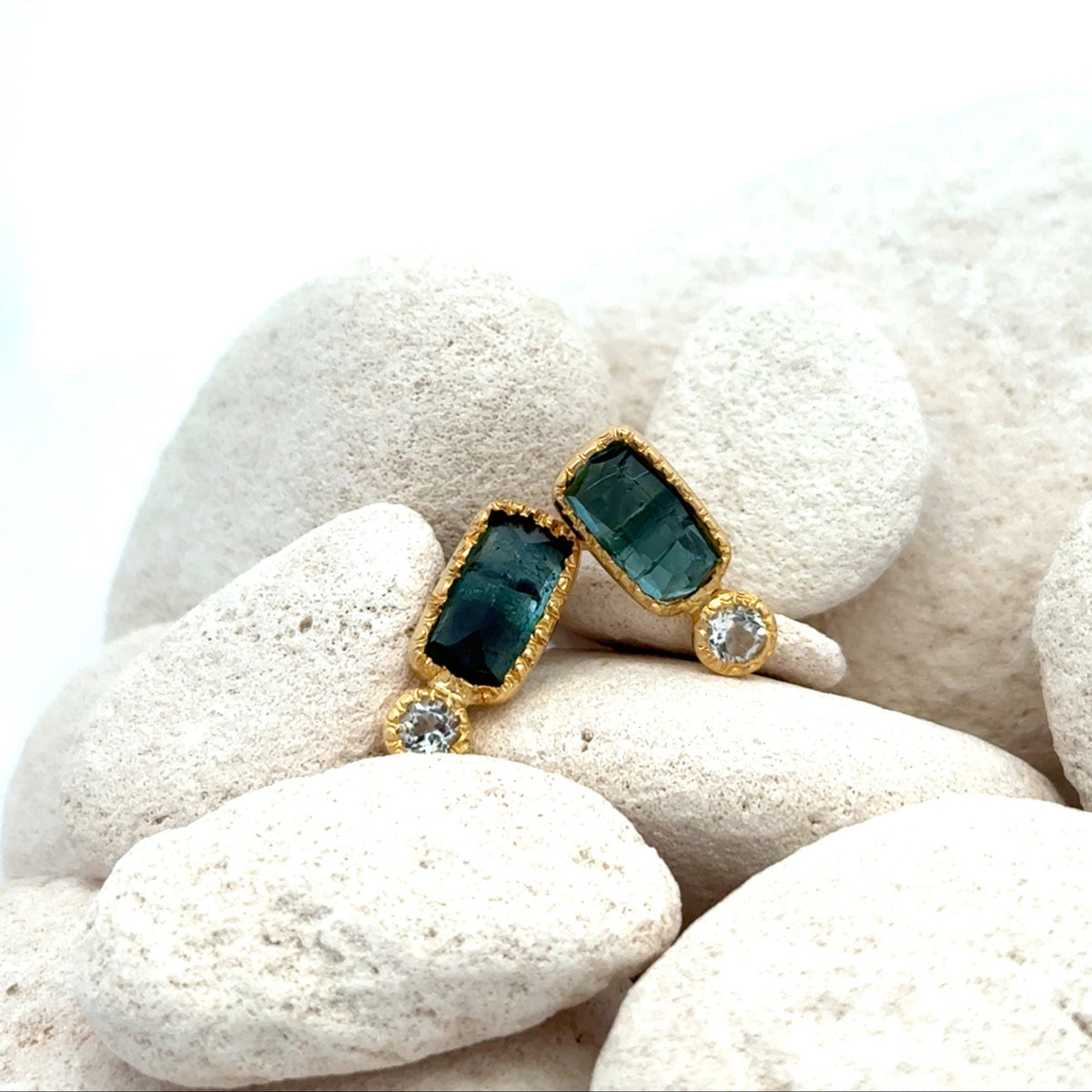 A pair of gold earrings with rectangular aquamarine gemstones and diamond accent stones, displayed on white decorative stones against a bright white background.