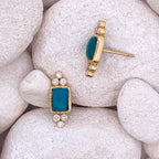 Gold and teal earrings on white stones