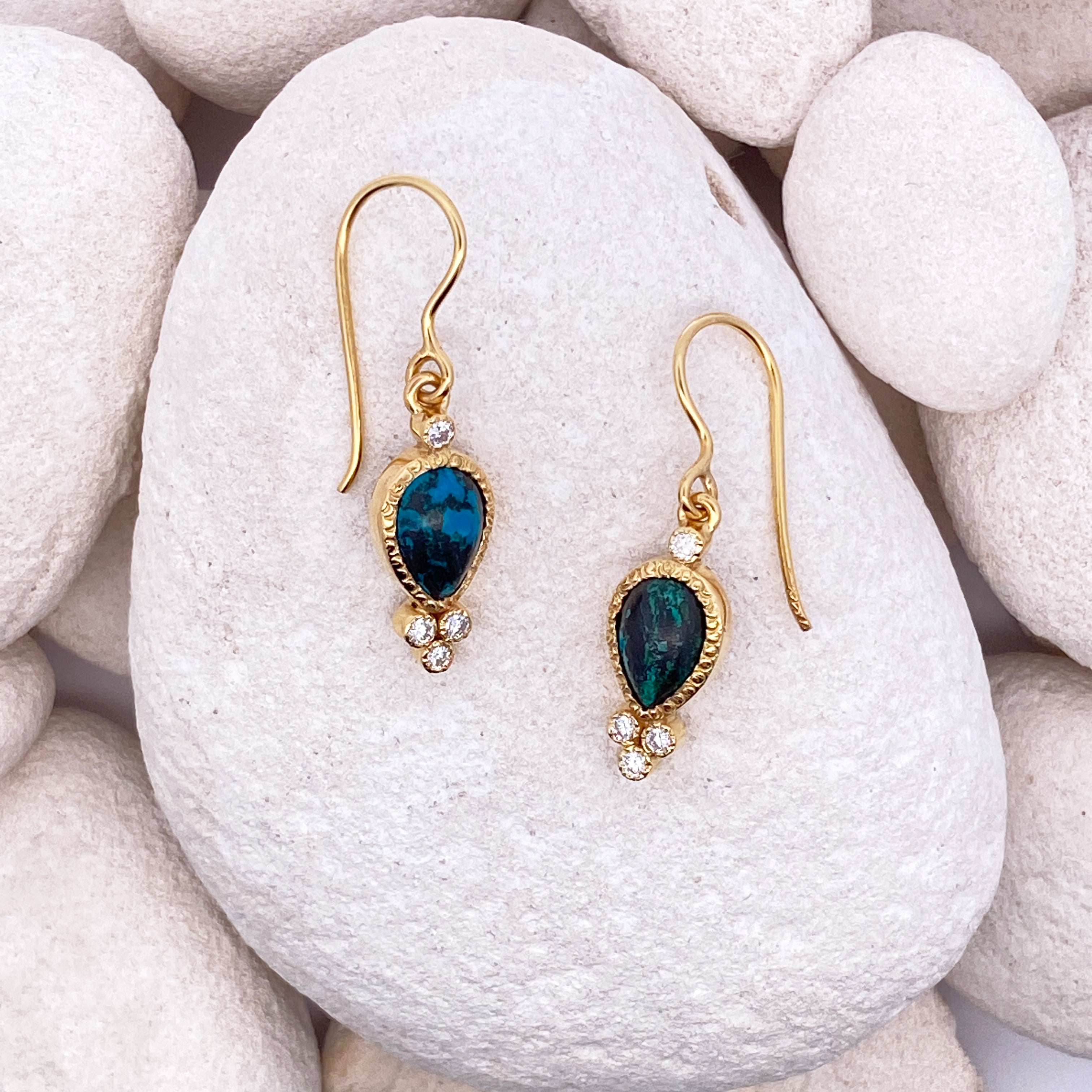 Gold earrings with blue gemstones on a rock.