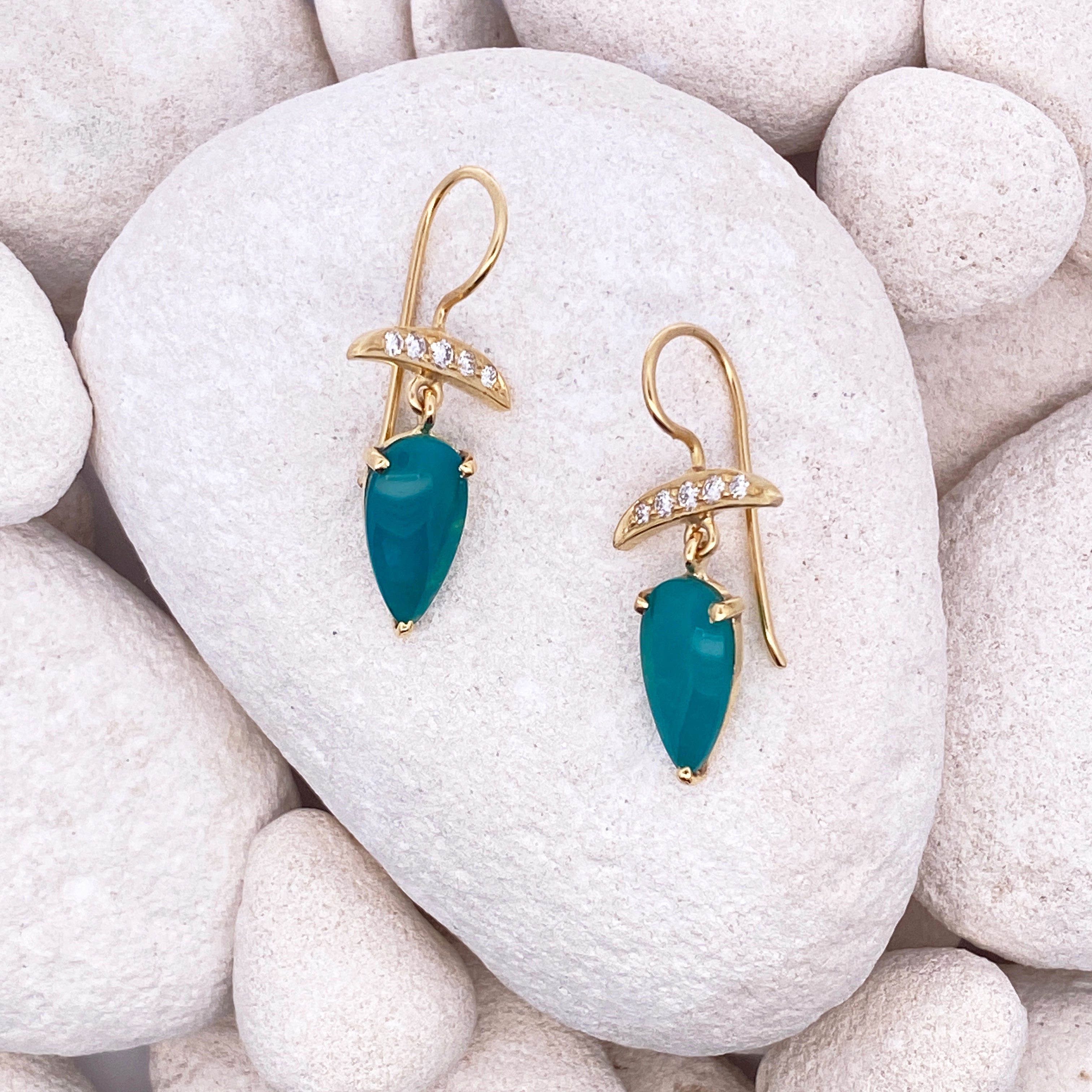 Gold earrings with green gemstones on a rock.
