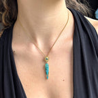 Gold necklace with a turquoise pendant on a person wearing a black top.