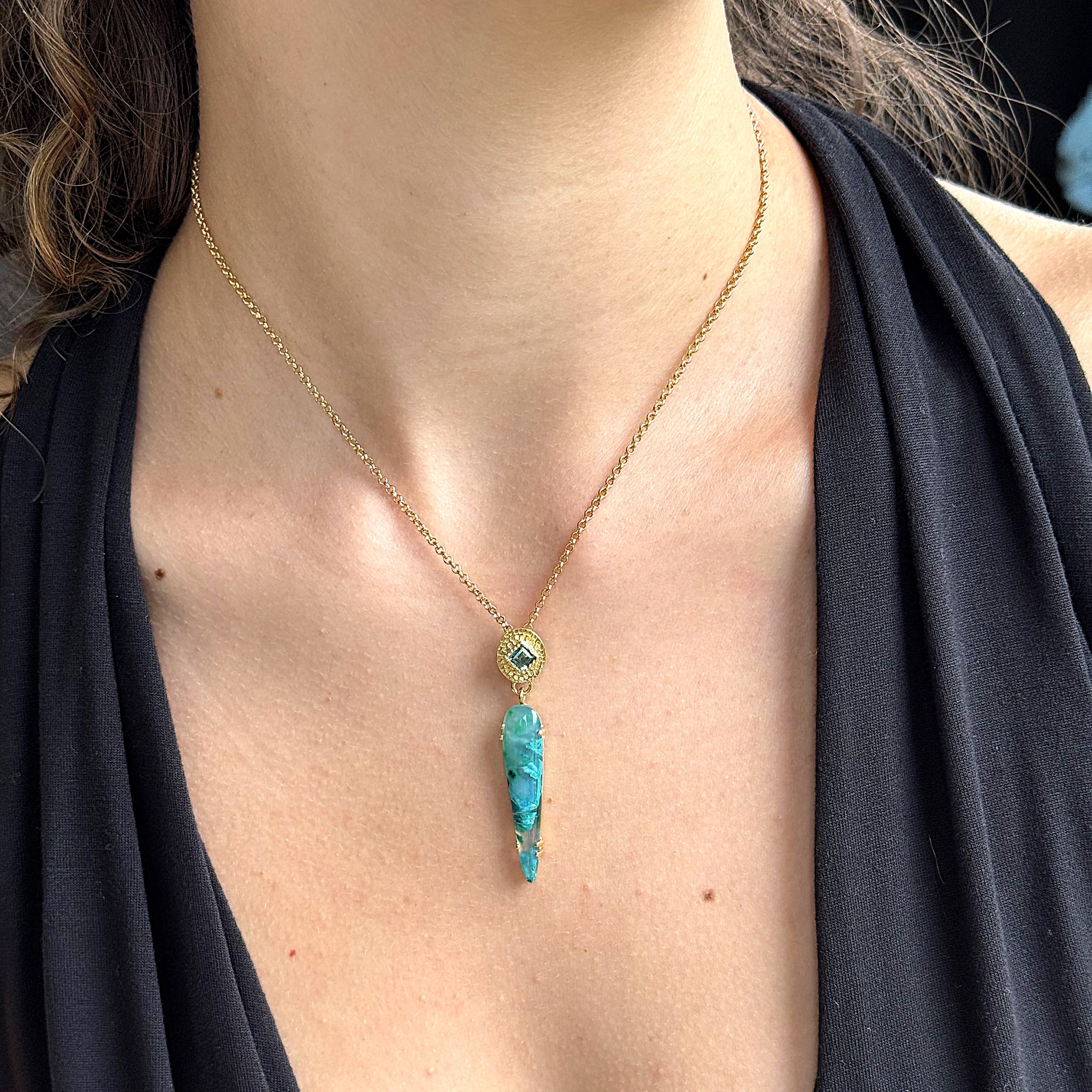 Gold necklace with a turquoise pendant on a person wearing a black top.