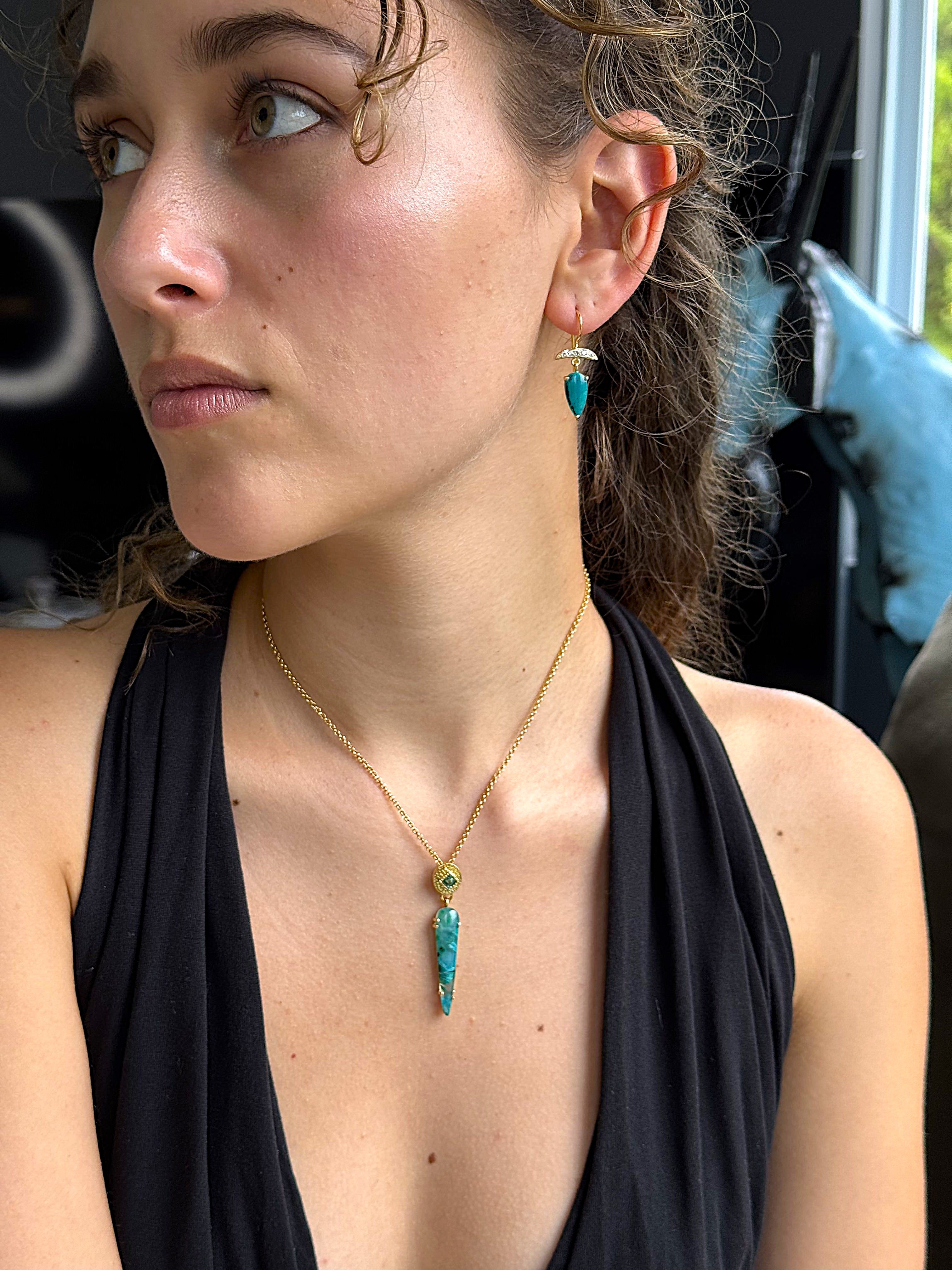 Woman wearing a black top and gold necklace with a turquoise pendant.
