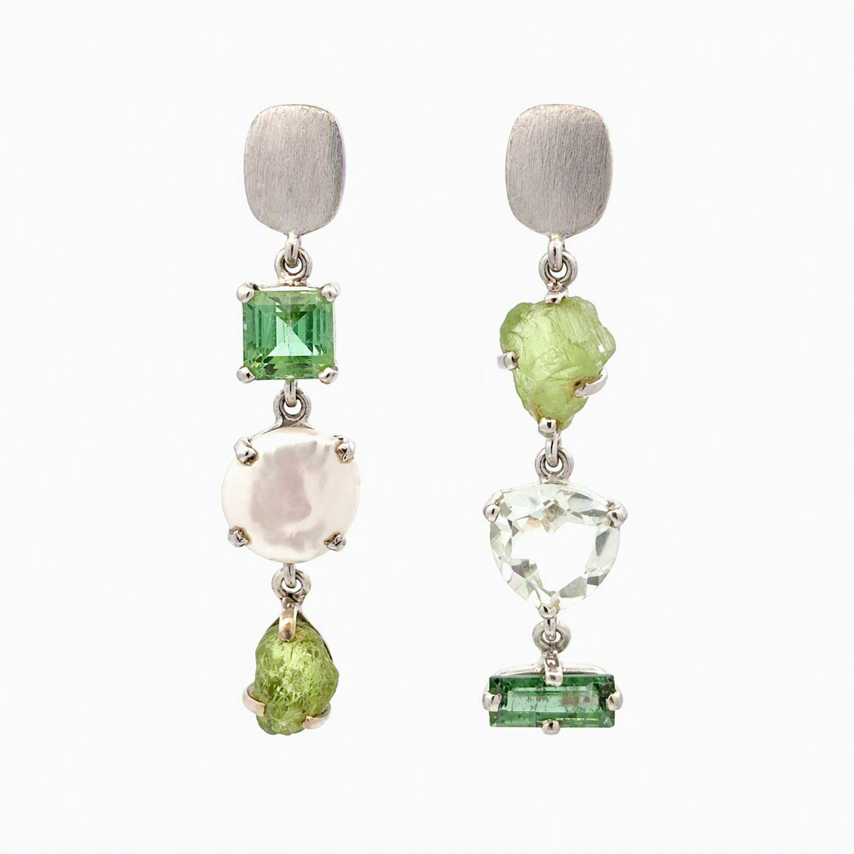 A pair of silver drop earrings featuring green gemstones, a white pearl, and rough peridot on a plain white background.