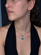 Close-up of a person wearing a gold necklace with a blue pendant.