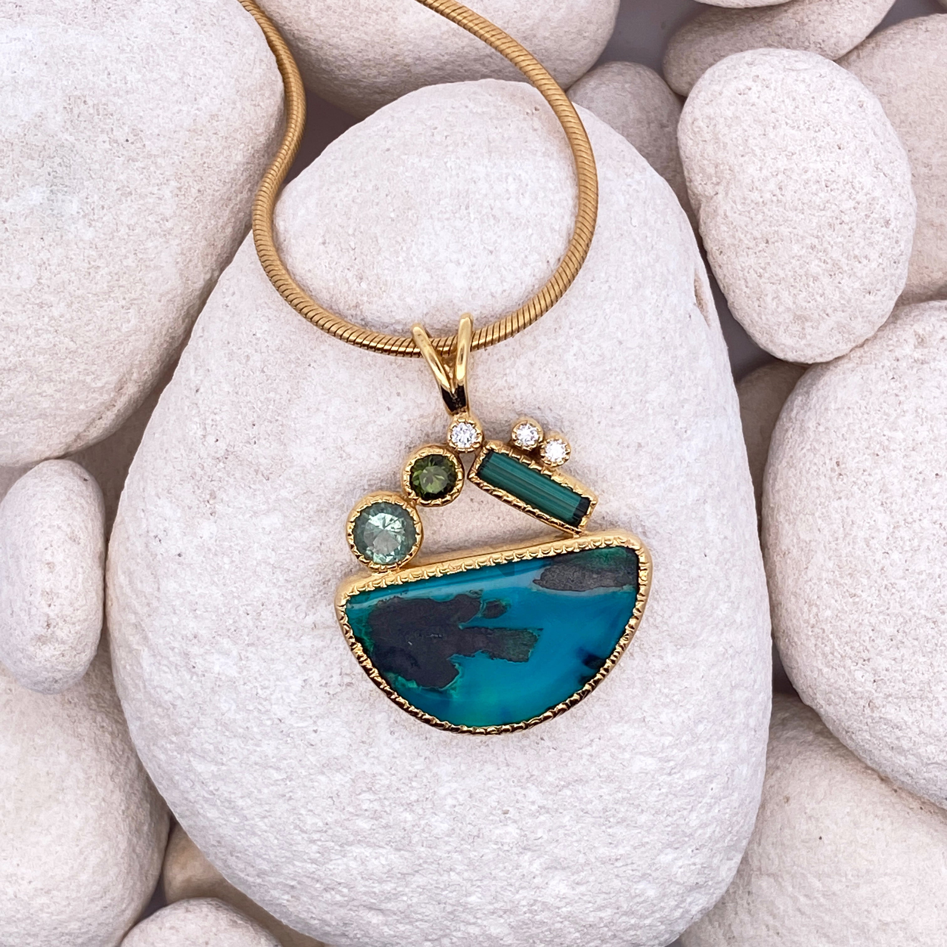 Gold necklace with a blue pendant on white pebbles.