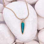 Gold necklace with a turquoise pendant on white pebbles