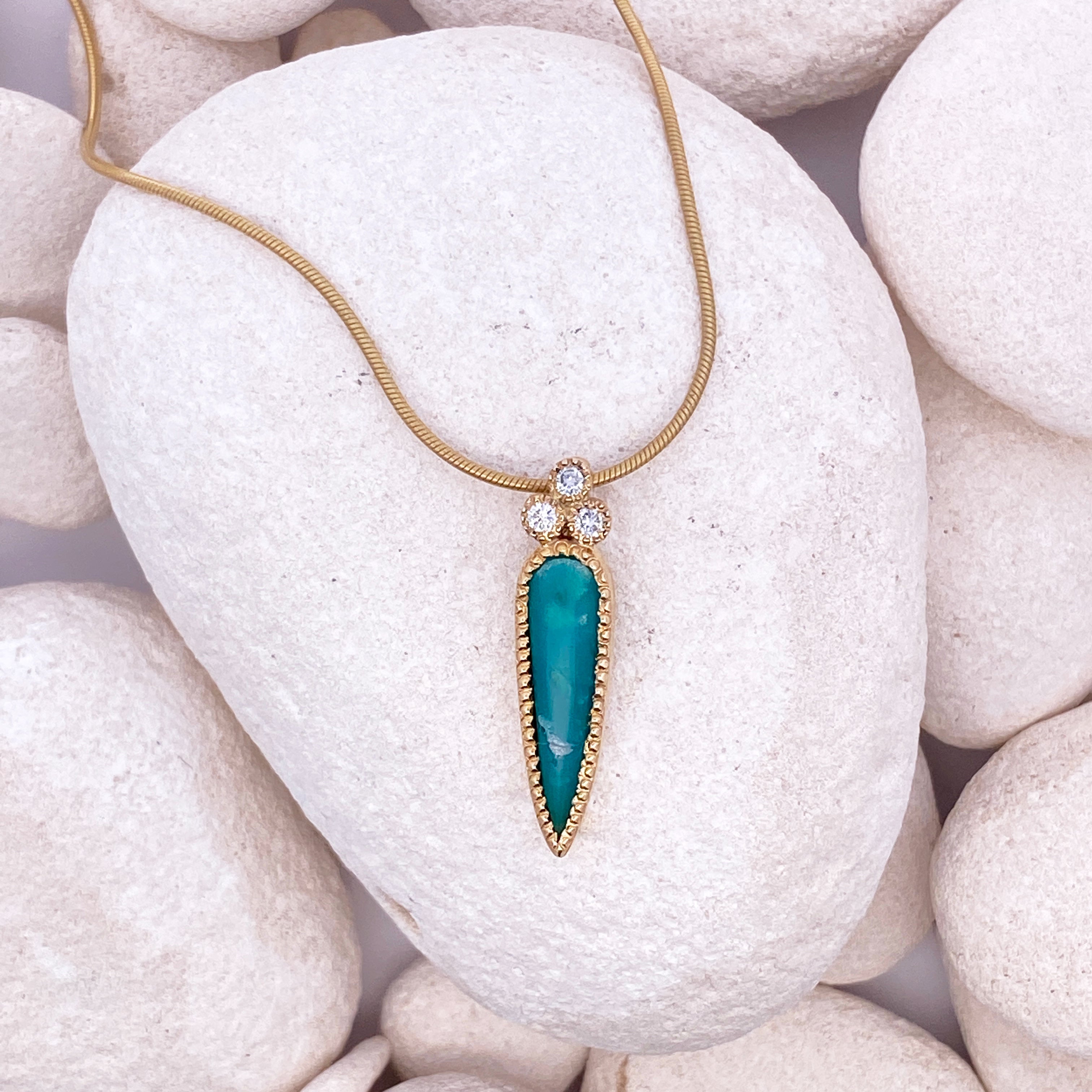 Gold necklace with a turquoise pendant on white pebbles