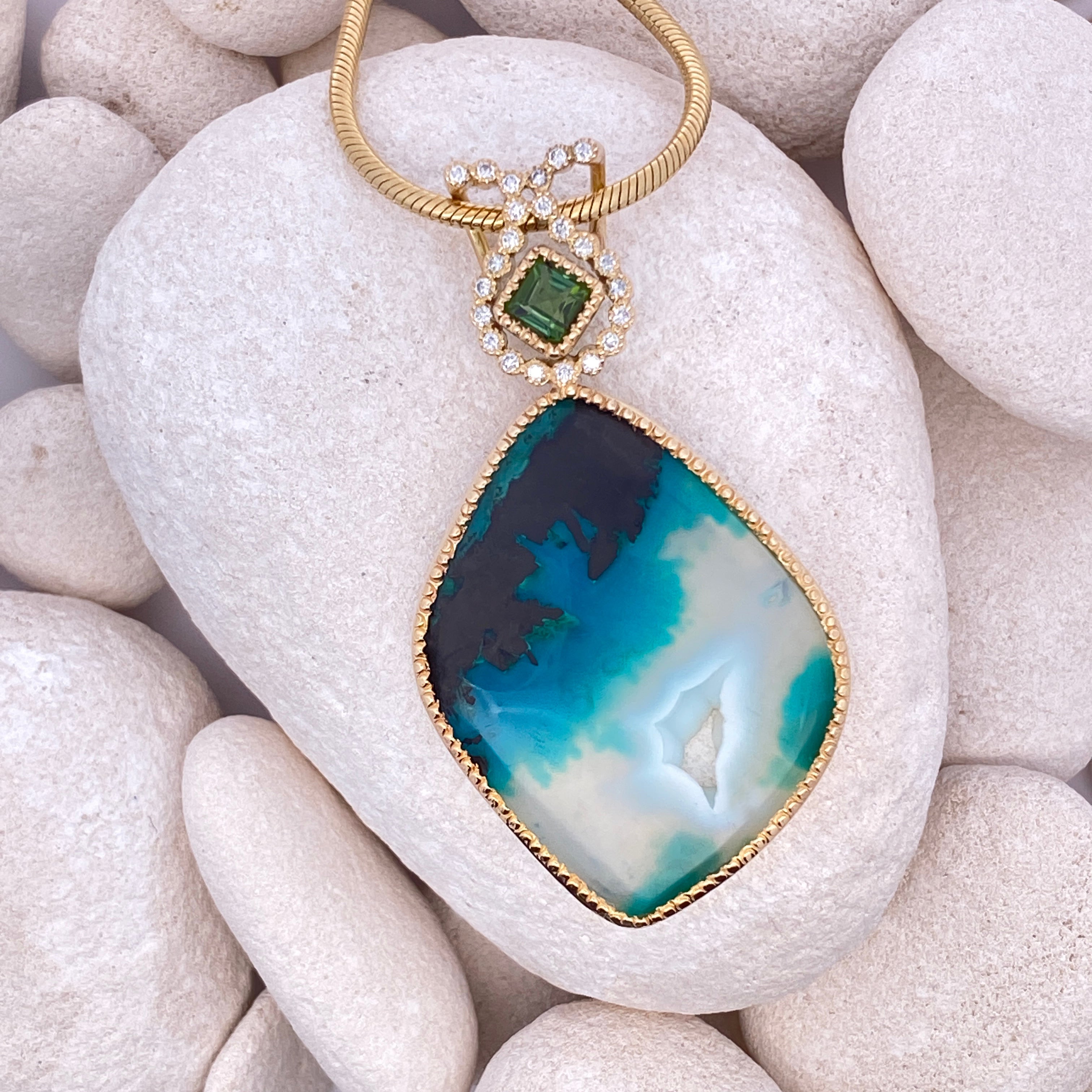 Gold necklace with a blue and green pendant on white stones