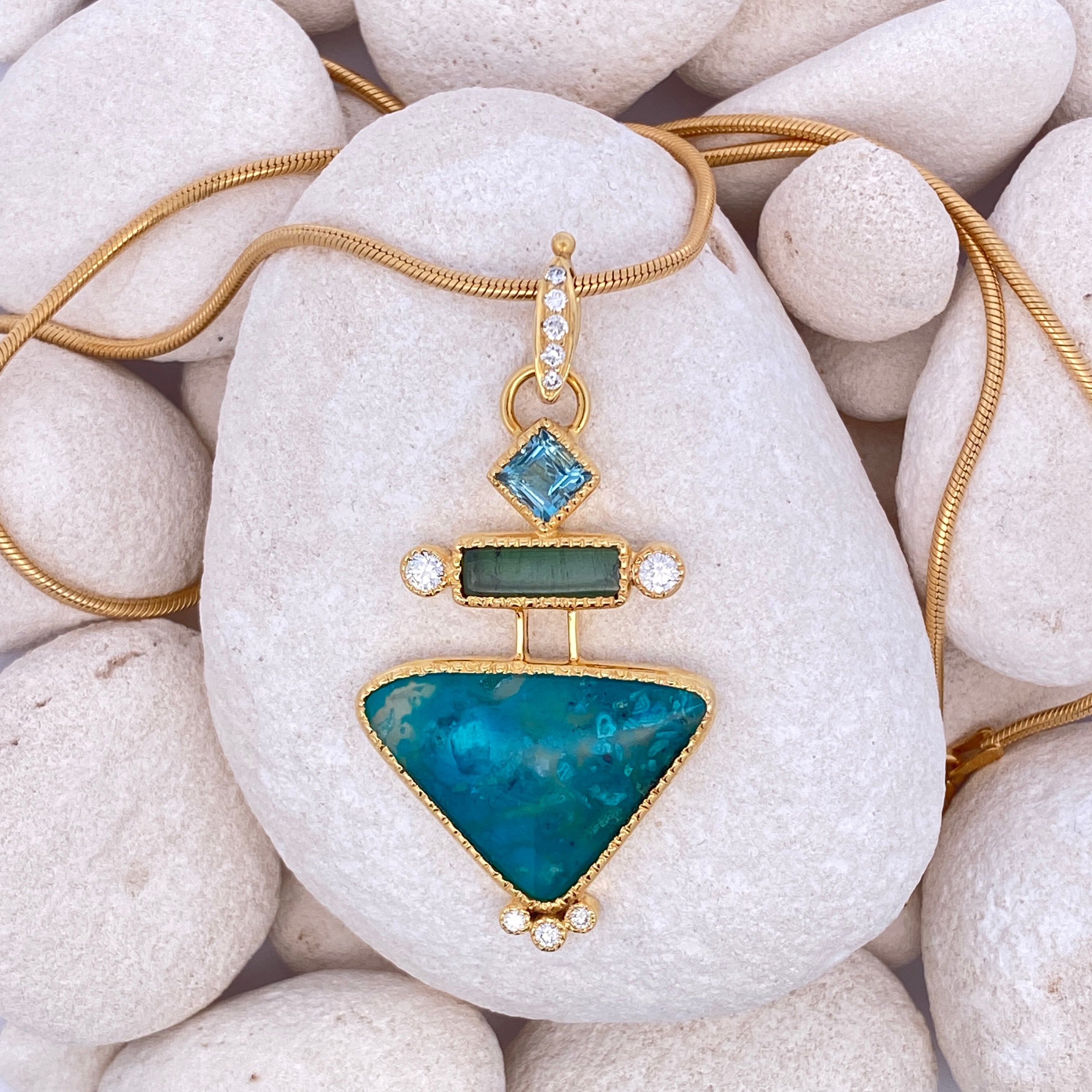 Gold necklace with a blue pendant on a rock.
