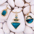 Three gold pendant necklaces with blue stones on white stones.