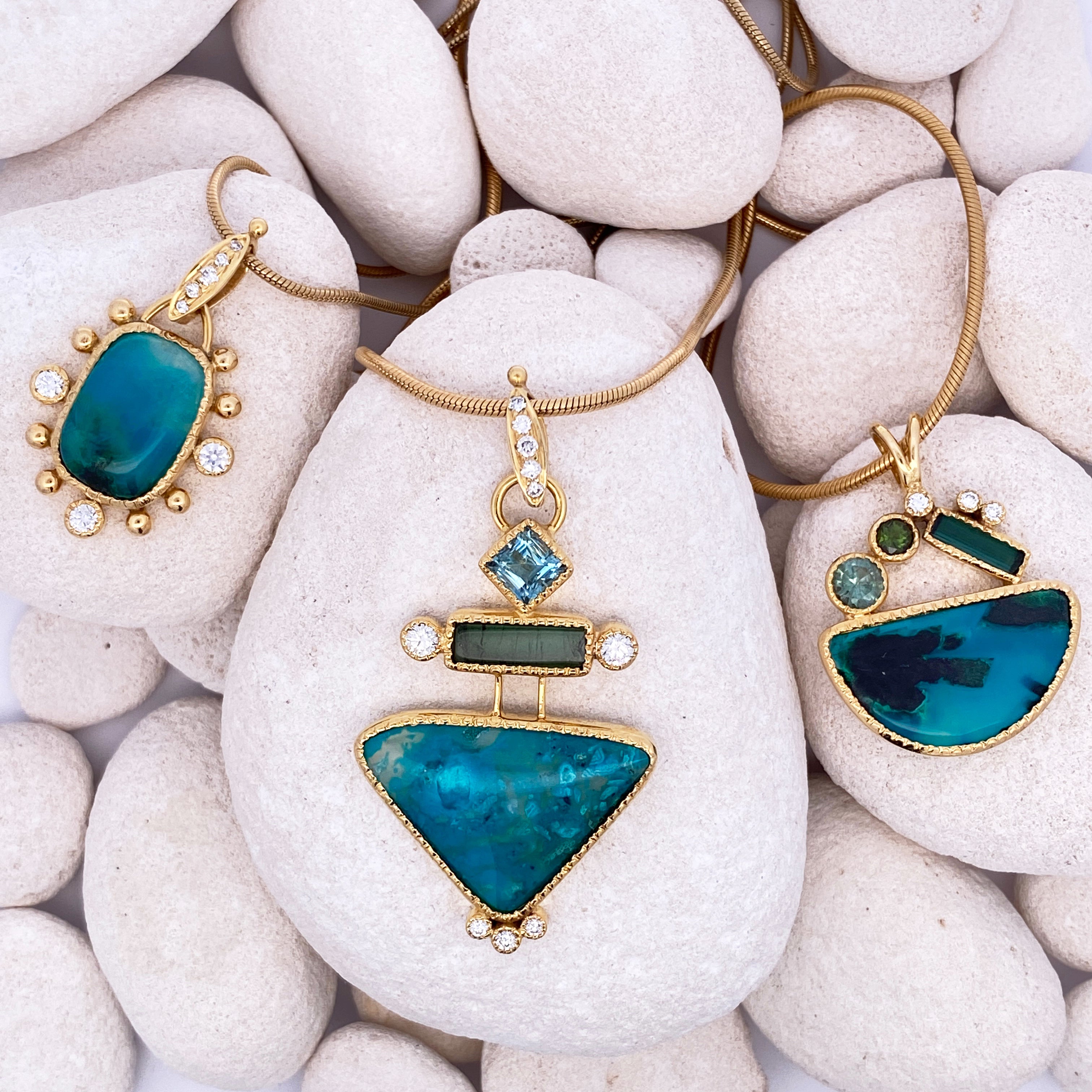 Three gold pendant necklaces with blue stones on white stones.