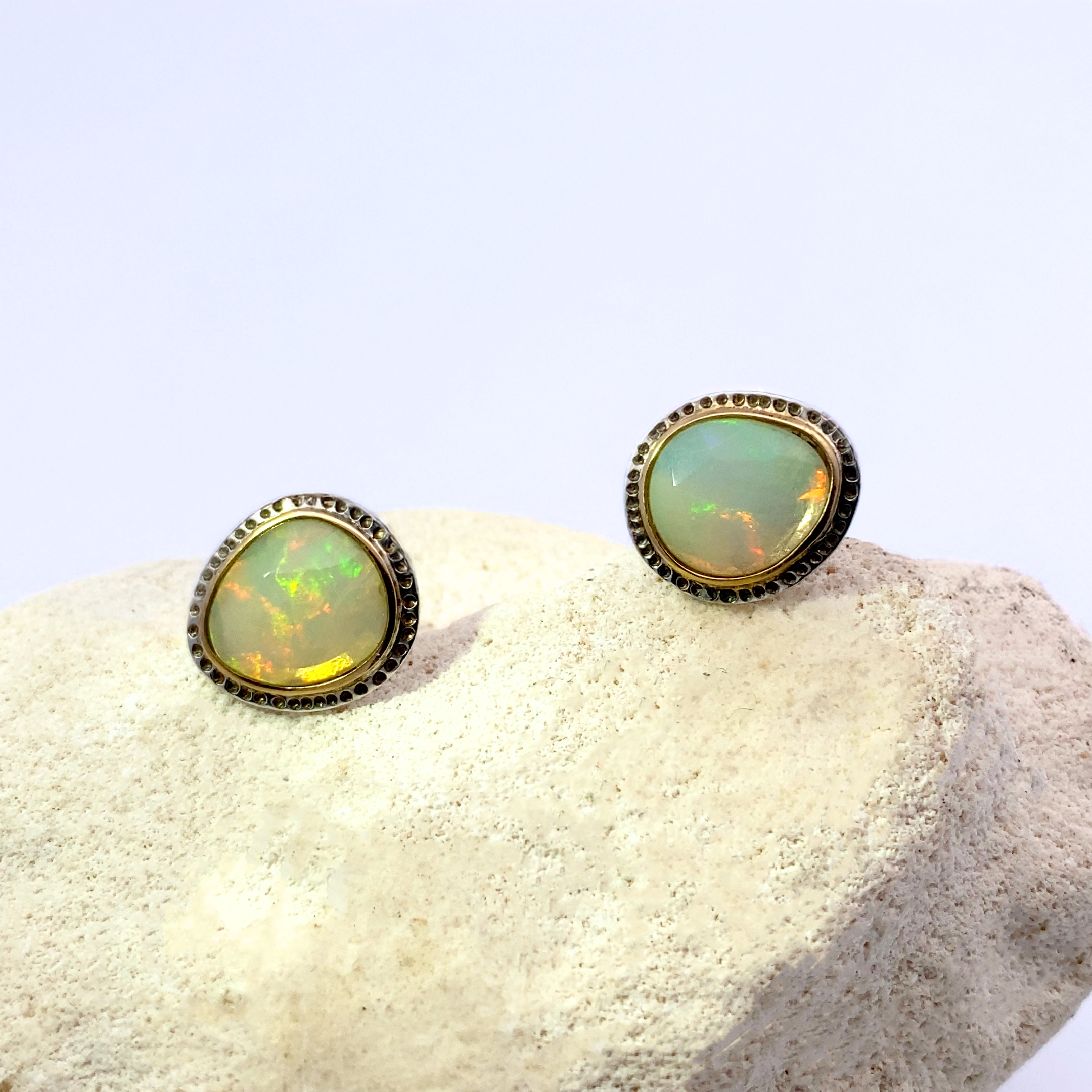 Opal stud earrings on a textured white surface with a light blue background