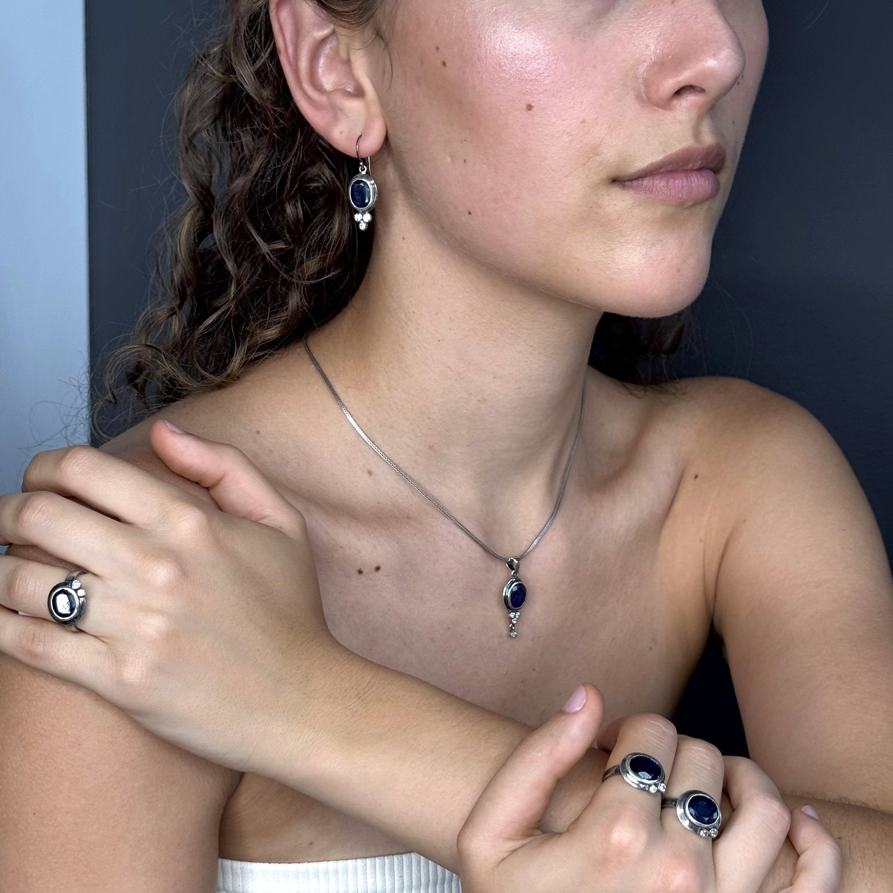 Close-up of a person wearing a necklace, earrings, and rings with a dark background
