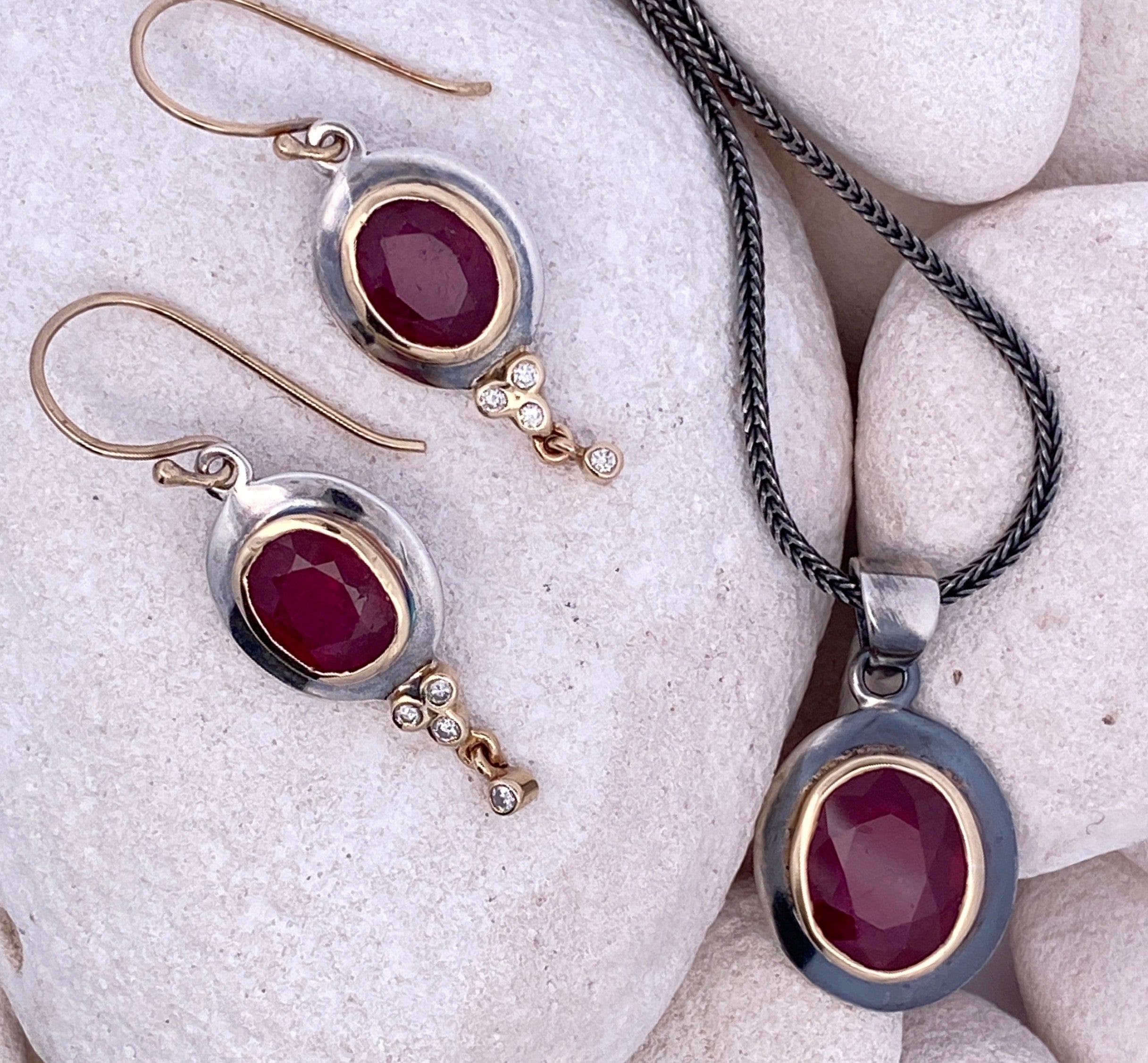 Jewelry set with red ruby gemstones with silver, gold, black, and diamond accents on white stones 