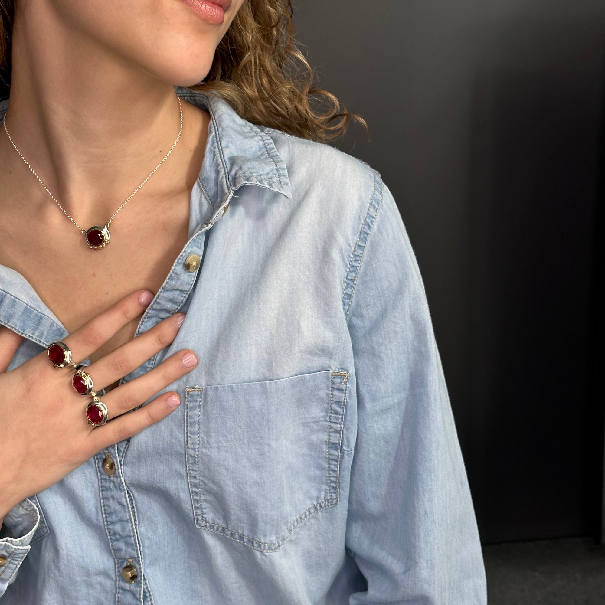 Person wearing a matching ruby with silver and 14k gold necklace and ring with a dark background