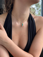 Person wearing a black top with a gold and green necklace, sitting outdoors.