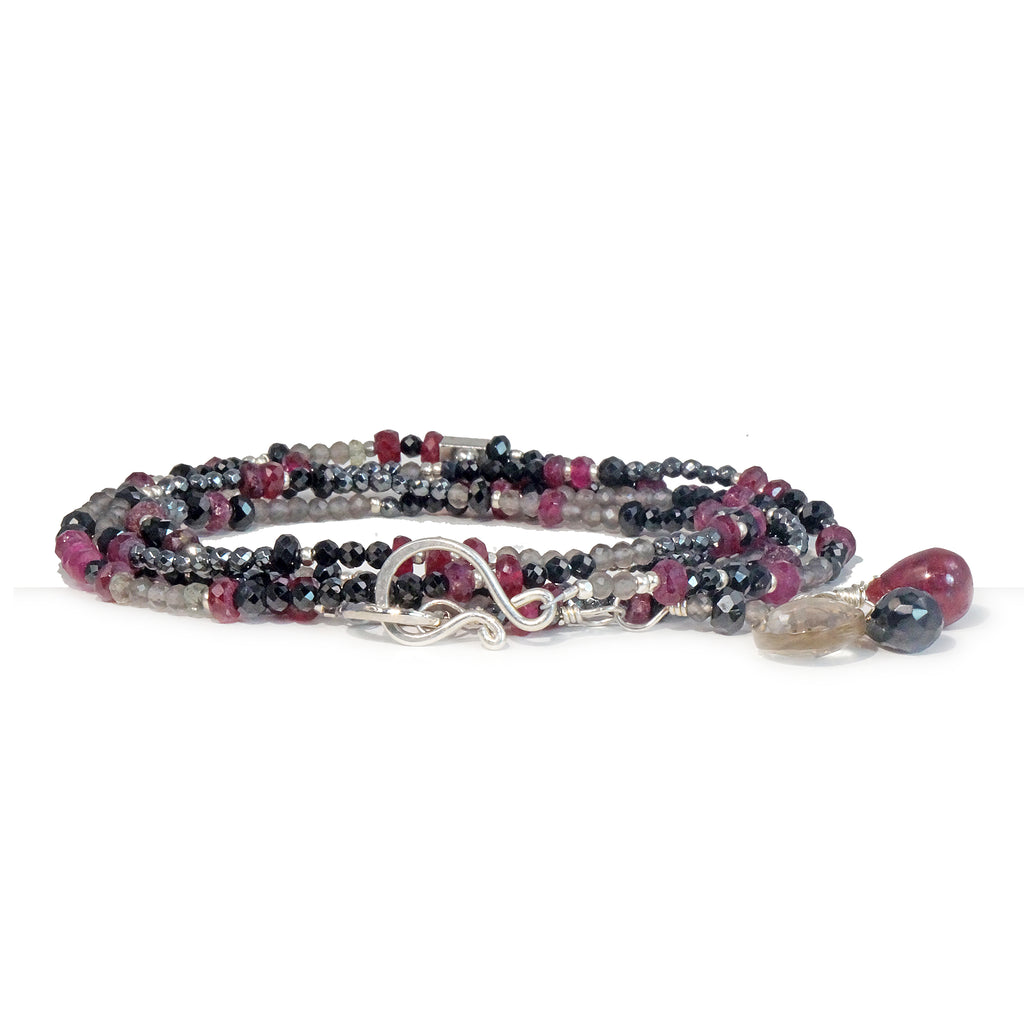 A multi-strand necklace with a silver clasp, featuring a variety of beads including rubies, spinels, hematite, labradorite, and grey topaz.