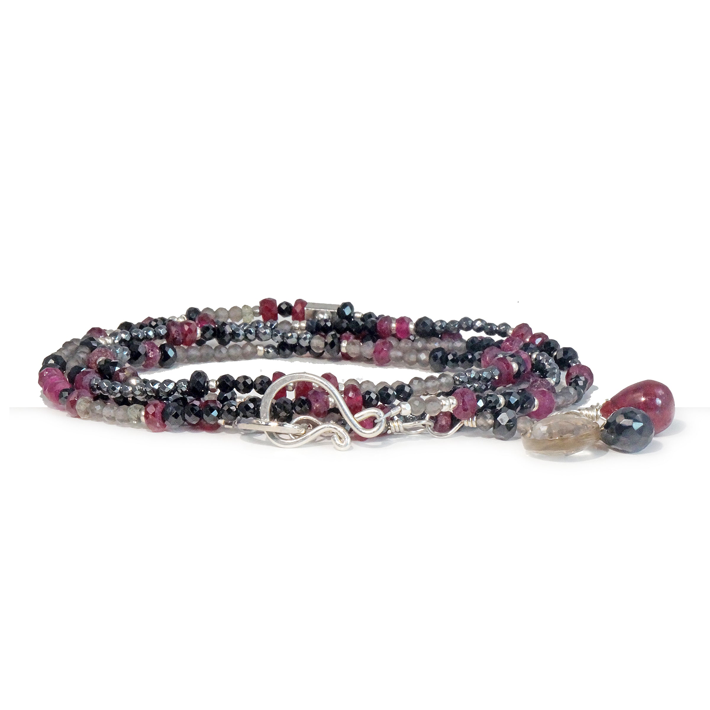 A multi-strand necklace with a silver clasp, featuring a variety of beads including rubies, spinels, hematite, labradorite, and grey topaz.