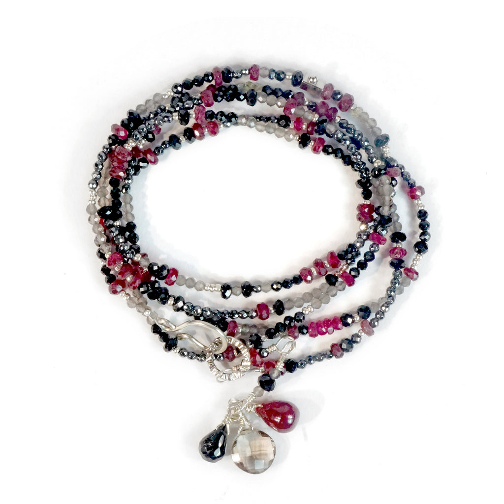 A multi-strand necklace with a silver clasp, featuring a variety of beads including rubies, spinels, hematite, labradorite, and grey topaz.